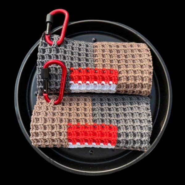Topflappen zusammengelegt und übereinander in eine Pfanne gelegt. Auf der oberen linken Seite sind je ein Karabienerhaken befestift. Die Farben sind grau, beige, rot, weiß. Das Muster besteht aus fünf Rechtecken, wo bei eines mittig umrandet von den anderen vier umrandet ist. Presine, im Shop Topflappen online kaufen.